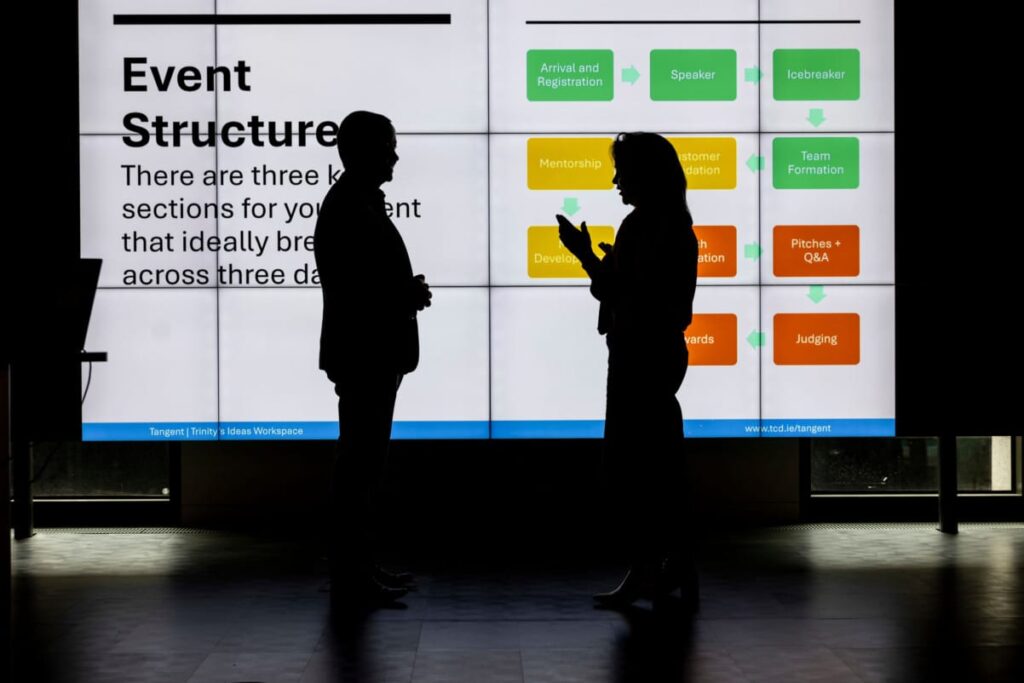 Silhouette of 2 people in front of a large screen outlining a plan for an event