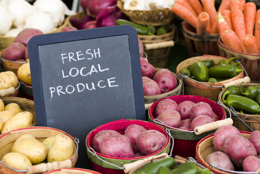 Chalkboard sign that says fresh local produce among vegetables on a market table